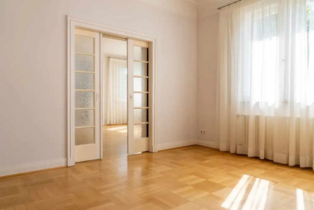 Ein heller leerer Raum mit Parkettboden, großen Fenstern und einer offenen Schiebetür in einem Haus in Waldhausen