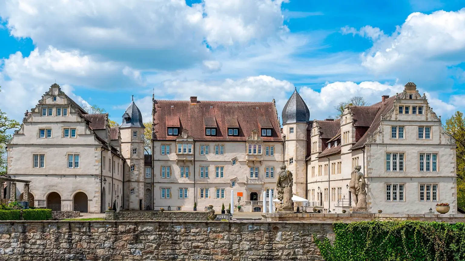 Zu sehen ist das Schloss Münchhausen im Stil der Weserrenaissance, aufgenommen aus der Frontalperspektive. Die detailreiche Fassade mit typischen Renaissance-Elementen und die repräsentative Architektur dominieren das Bild