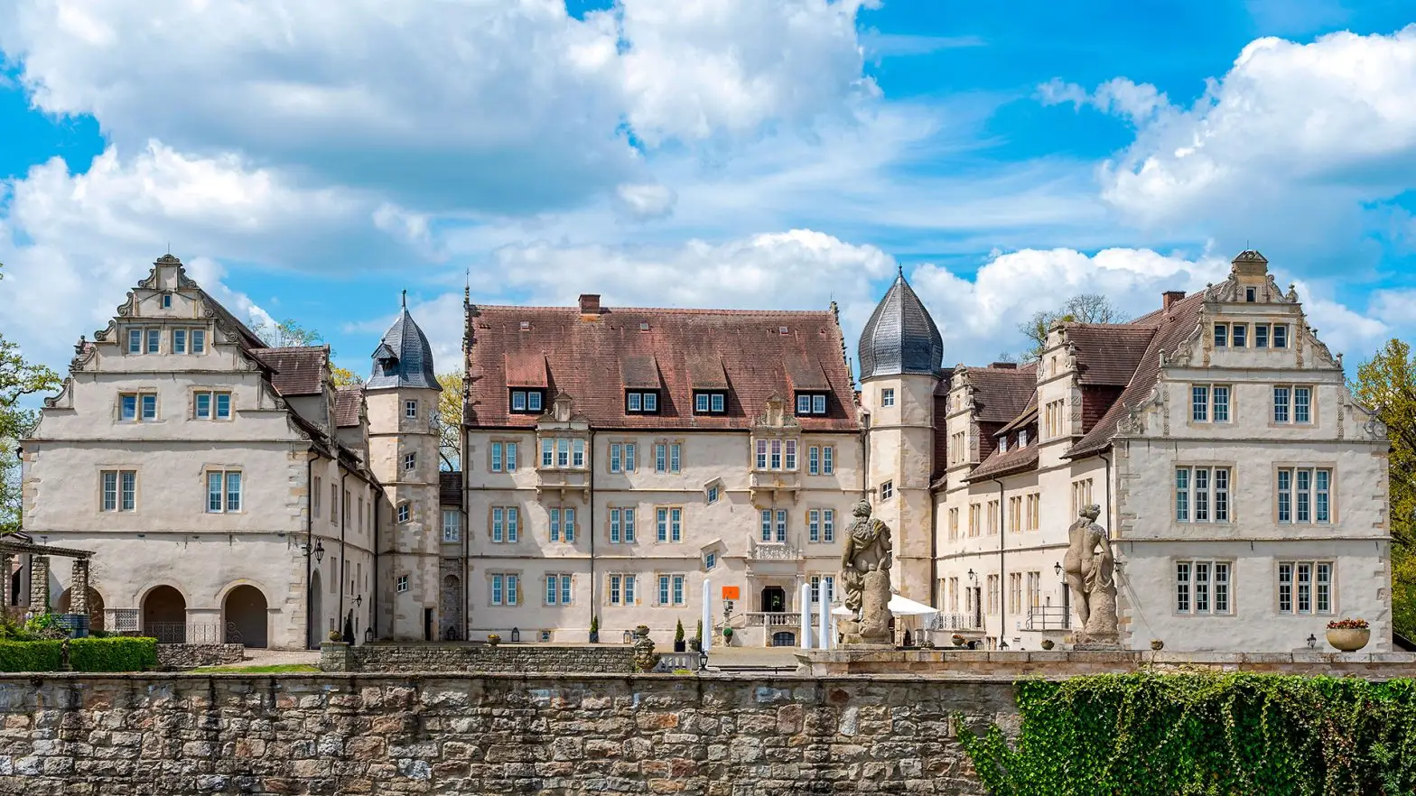 Zu sehen ist das Schloss Münchhausen im Stil der Weserrenaissance, aufgenommen aus der Frontalperspektive. Die detailreiche Fassade mit typischen Renaissance-Elementen und die repräsentative Architektur dominieren das Bild